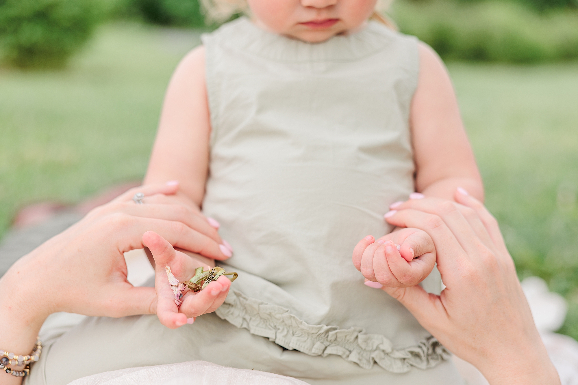 parents hold baby's hands while she sits on blanket 