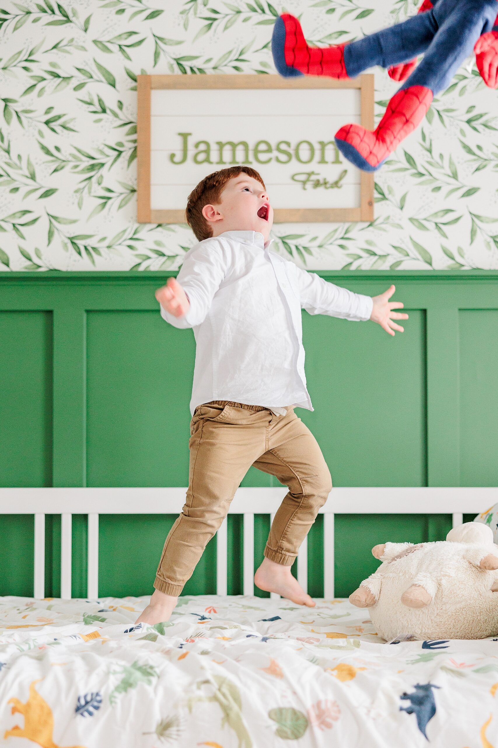 toddler jumps on bed tossing Spiderman toy in the air 