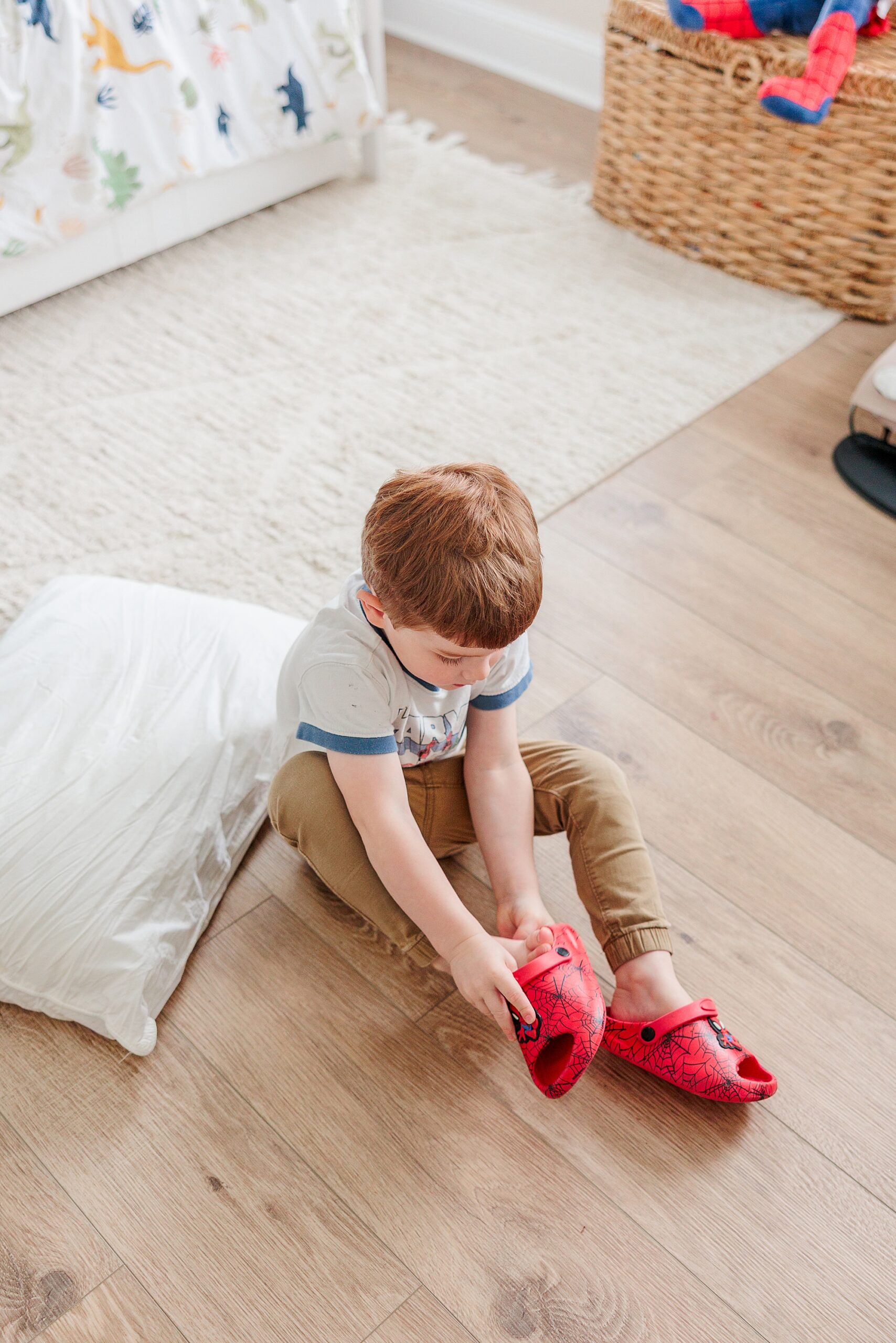 boy puts on red shoes sitting on wooden floor 
