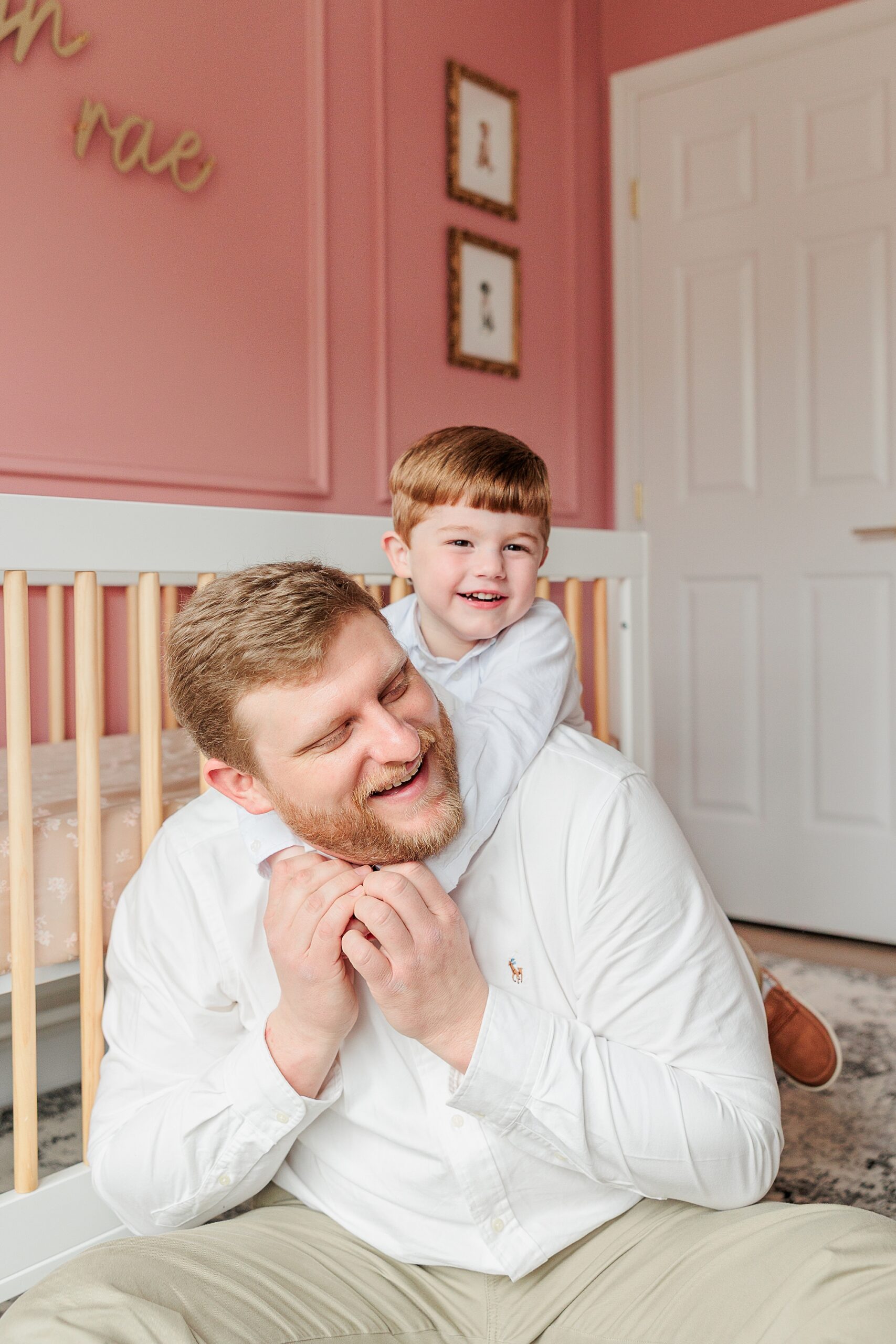 boy hugs dad from behind around the neck in sister's nursery