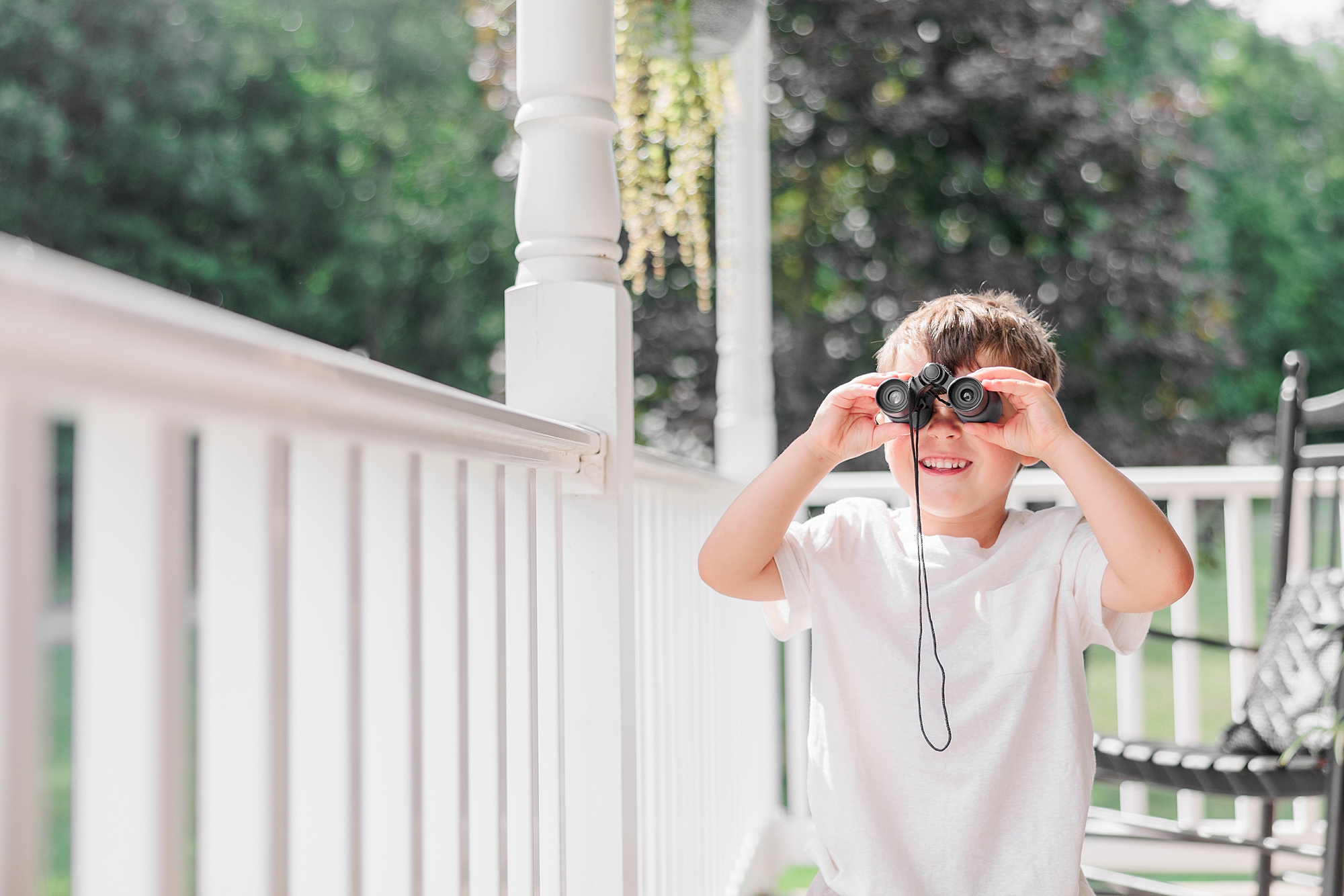 boy stands on porch looking through binoculars during family photos 