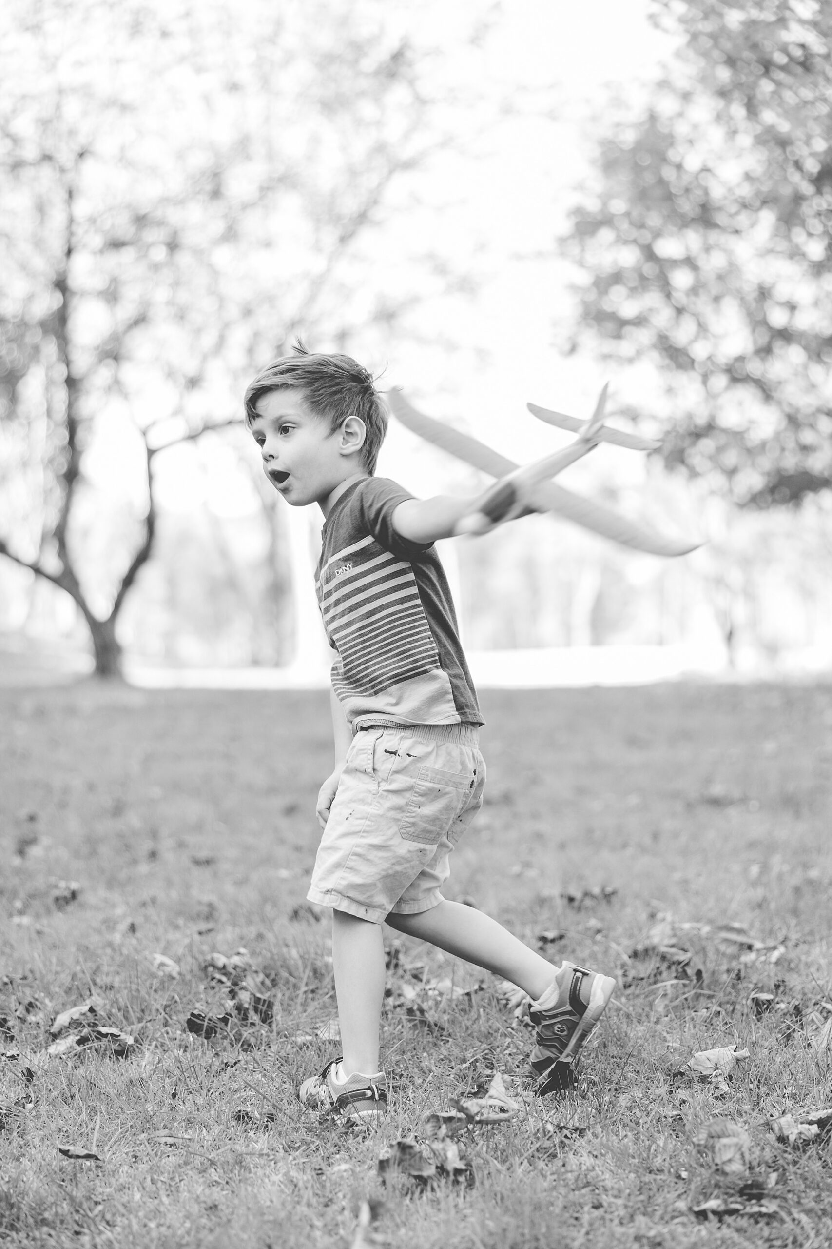 black and white photo of boy playing with airplane in yard
