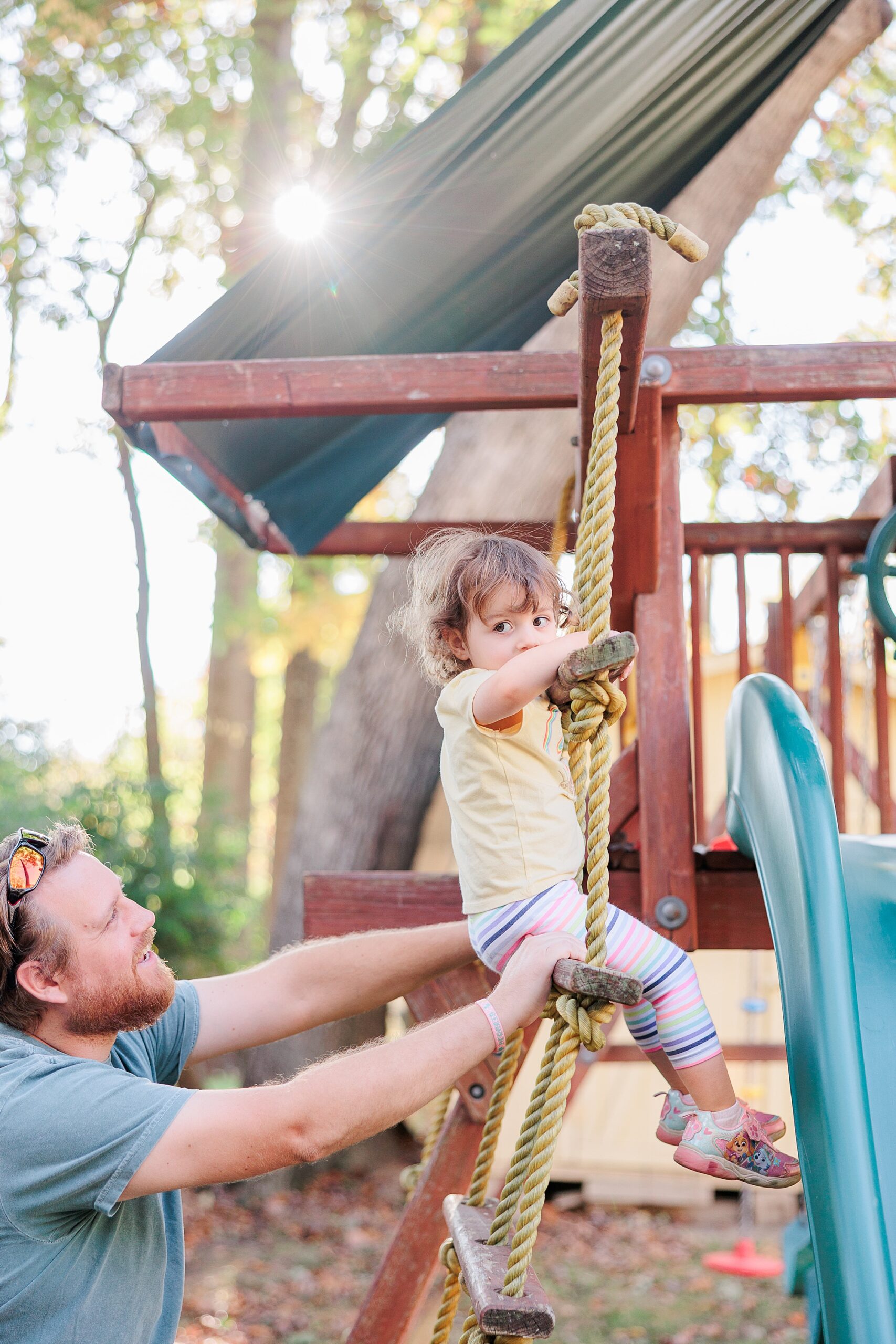 dad helps son climb up playground in backyard